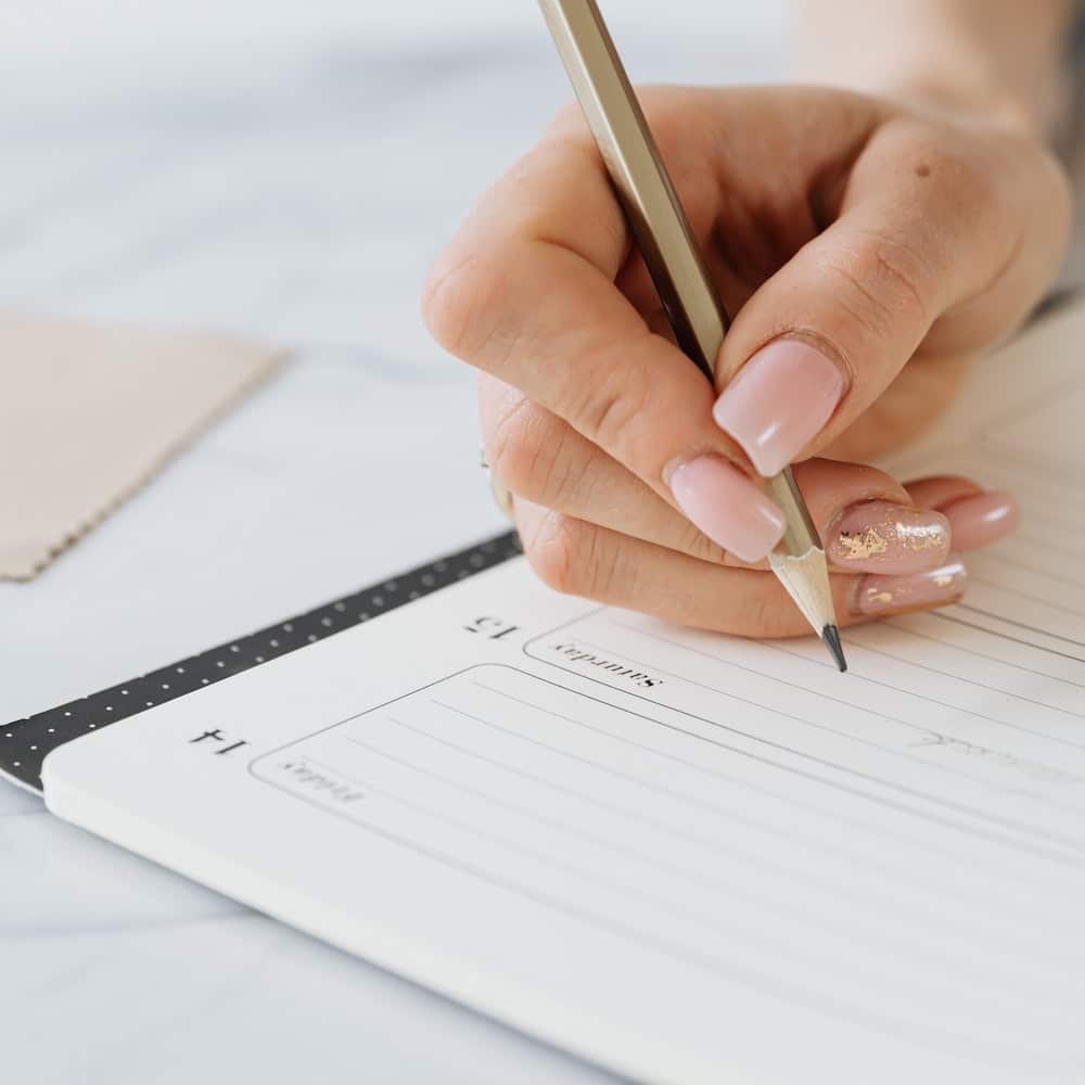 Woman's hand writing in a planner with a pencil